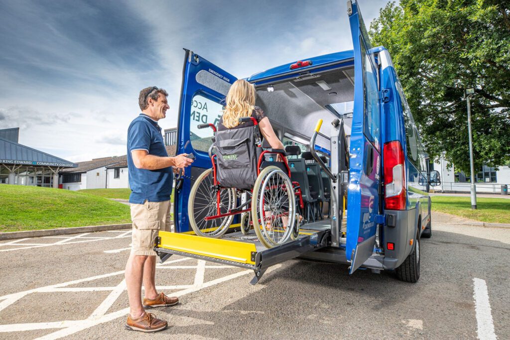 A wheelchair user is being lifted into the back of a minibus.