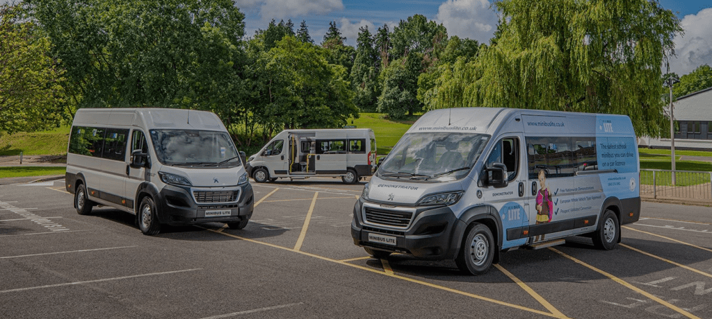 Three school minibuses parked in a car park on leafy school grounds.