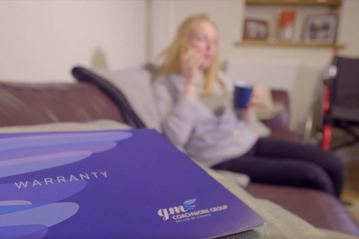 Warranty booklet in the foreground with a woman in the background holding a hot drink.